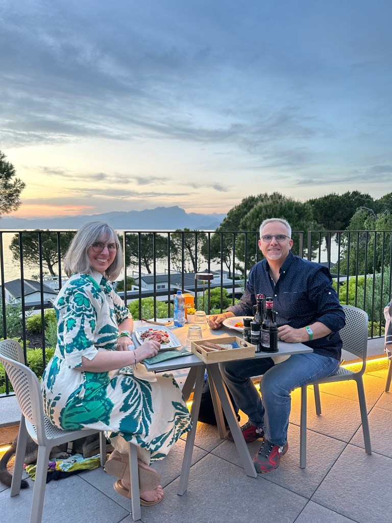 A couple enjoying dinner on a terrace restaurant by the lake at sunset, surrounded by nature and a beautiful view.