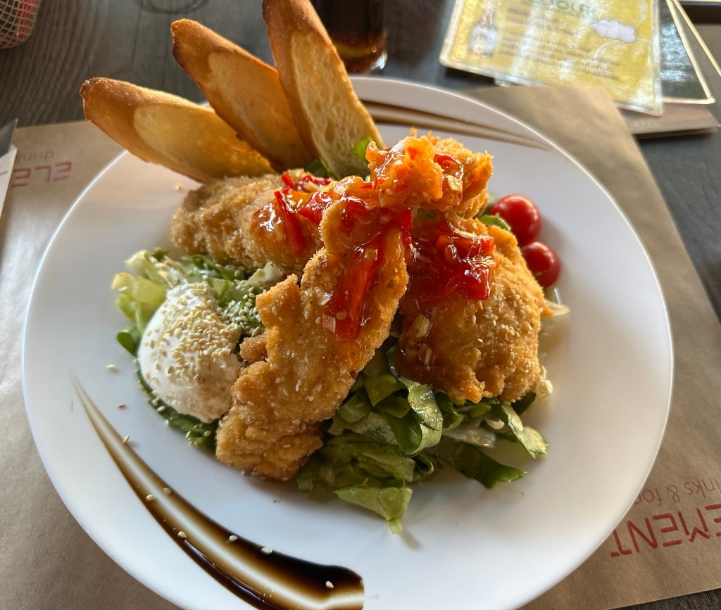 A plate of salad topped with fried chicken strips, red sauce, cherry tomatoes, and served with slices of toast.